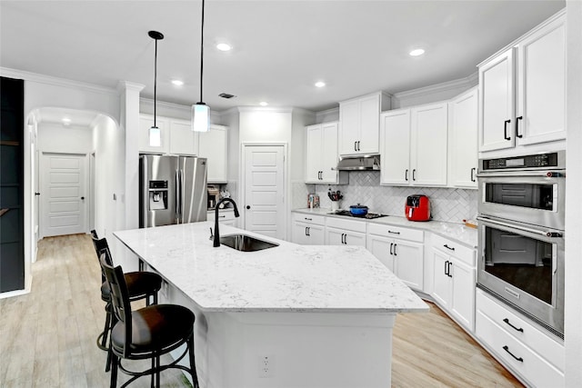 kitchen featuring pendant lighting, stainless steel appliances, an island with sink, and white cabinets