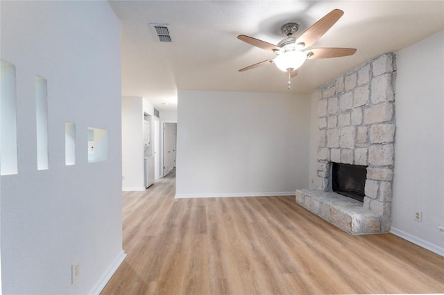 unfurnished living room with ceiling fan, a stone fireplace, and light hardwood / wood-style floors