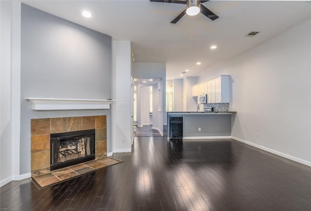 living room featuring a tiled fireplace, ceiling fan, and dark hardwood / wood-style flooring