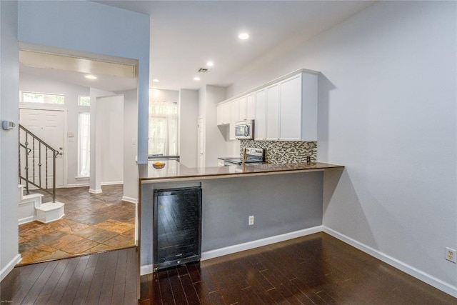 kitchen featuring appliances with stainless steel finishes, white cabinetry, wine cooler, decorative backsplash, and kitchen peninsula