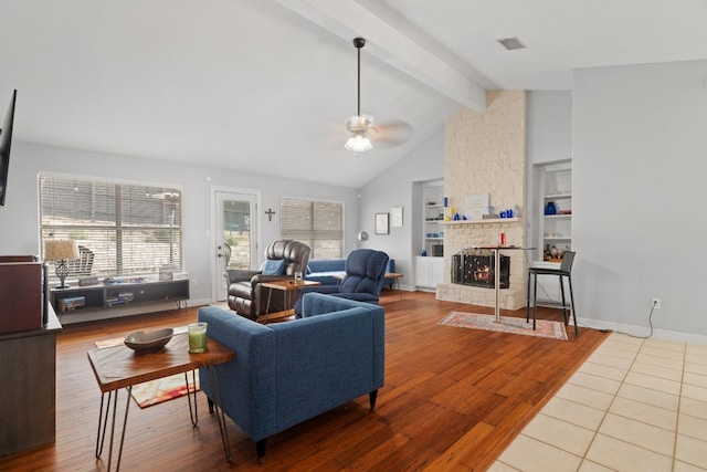 living room featuring a stone fireplace, built in features, hardwood / wood-style flooring, ceiling fan, and beam ceiling