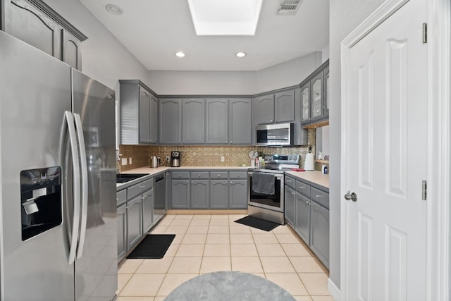 kitchen with gray cabinetry, light tile patterned floors, a skylight, and appliances with stainless steel finishes