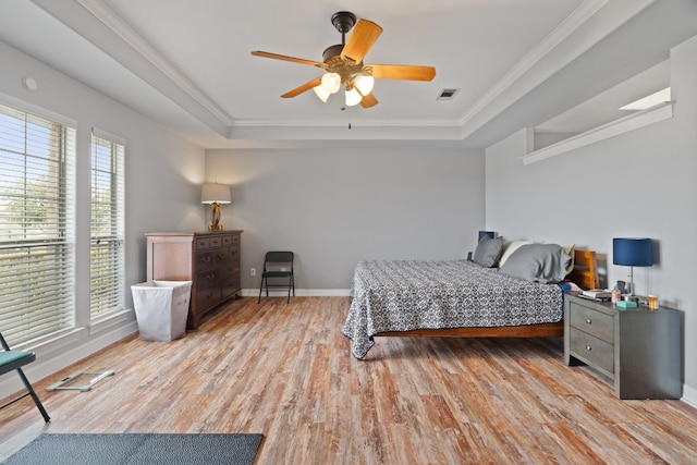 bedroom featuring ceiling fan, ornamental molding, a tray ceiling, and light wood-type flooring