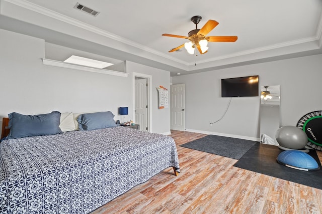 bedroom with hardwood / wood-style flooring, ornamental molding, ceiling fan, and a tray ceiling