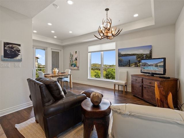 living room featuring a raised ceiling, ornamental molding, a chandelier, and dark hardwood / wood-style flooring