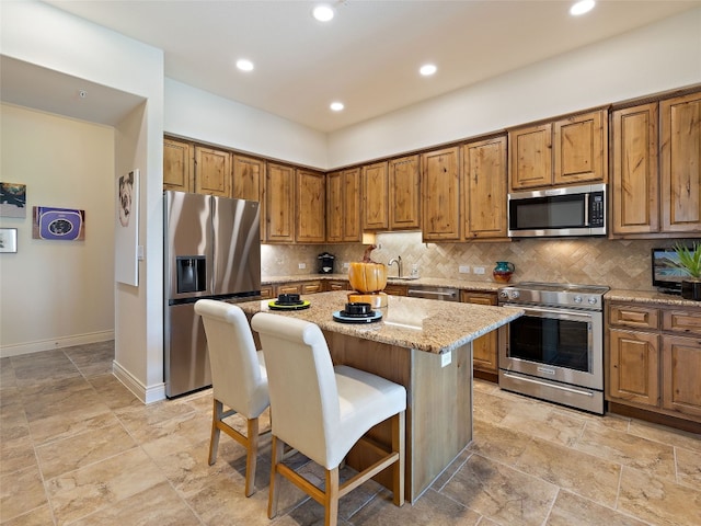 kitchen with sink, stainless steel appliances, a center island, light stone counters, and decorative backsplash