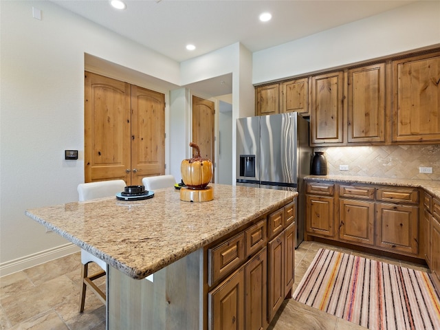 kitchen featuring tasteful backsplash, light stone countertops, a kitchen island, and a kitchen bar