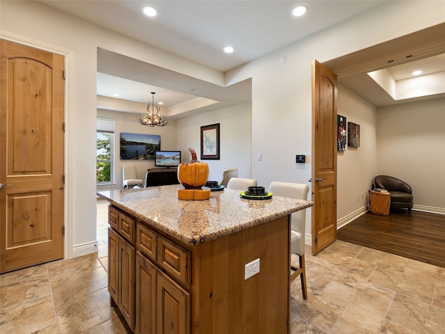 kitchen featuring a breakfast bar area, hanging light fixtures, light stone counters, a tray ceiling, and a kitchen island