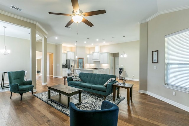 living room featuring dark hardwood / wood-style flooring, ceiling fan with notable chandelier, and ornamental molding