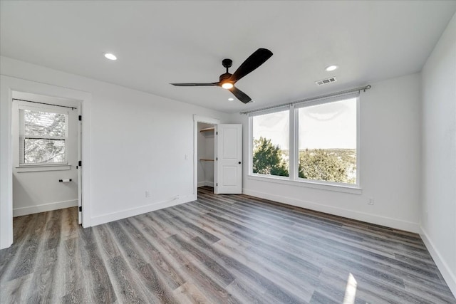 unfurnished bedroom featuring multiple windows, a walk in closet, light hardwood / wood-style floors, and ceiling fan