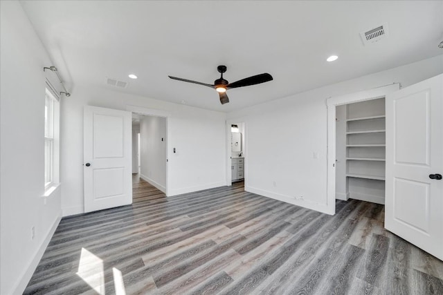 unfurnished bedroom with ceiling fan, a walk in closet, wood-type flooring, and a closet