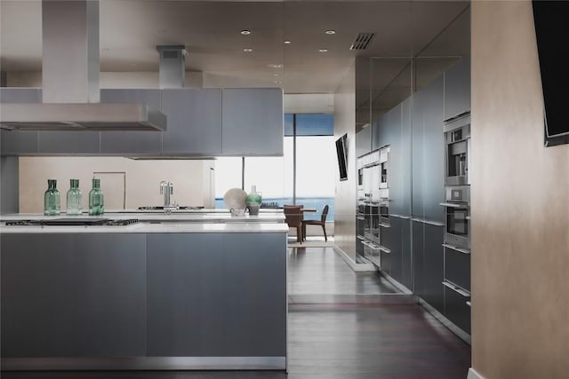 kitchen featuring dark wood-type flooring, gray cabinets, gas stovetop, island exhaust hood, and oven