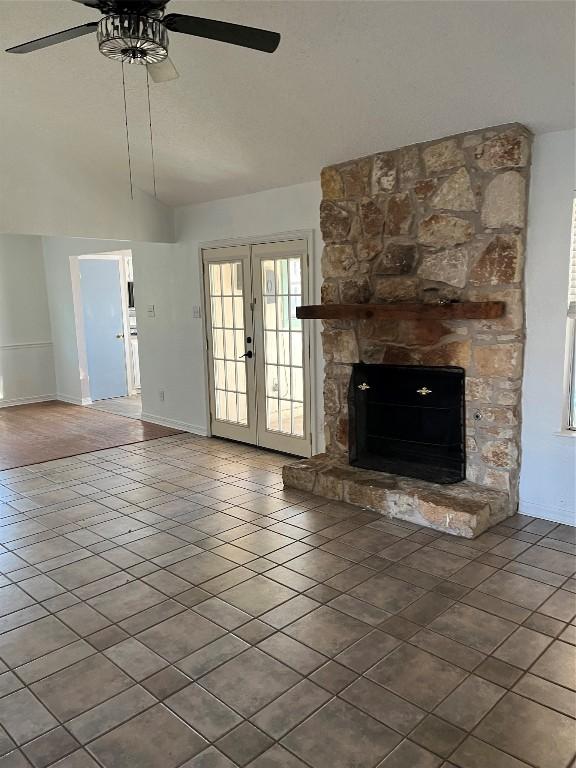 unfurnished living room with vaulted ceiling, a stone fireplace, ceiling fan, tile patterned floors, and french doors