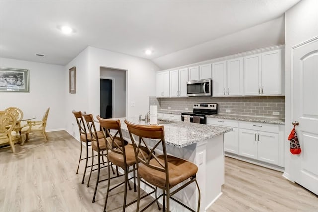 kitchen with stainless steel appliances, light stone countertops, a breakfast bar area, and white cabinets