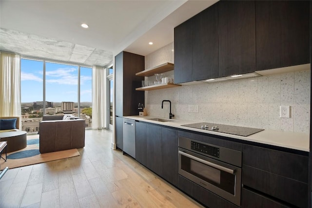 kitchen with sink, a wall of windows, stainless steel appliances, light hardwood / wood-style floors, and decorative backsplash