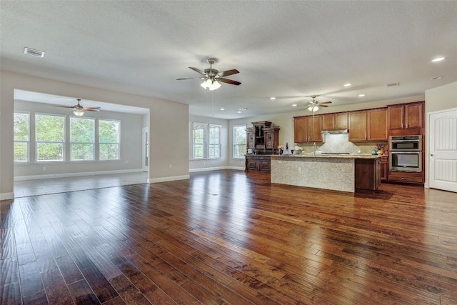 kitchen featuring tasteful backsplash, a center island with sink, a textured ceiling, dark hardwood / wood-style floors, and stainless steel double oven