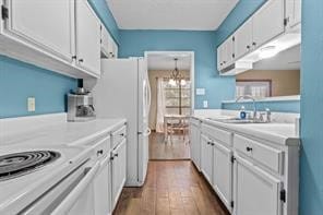 kitchen featuring dark wood-type flooring, sink, a chandelier, white fridge, and white cabinets