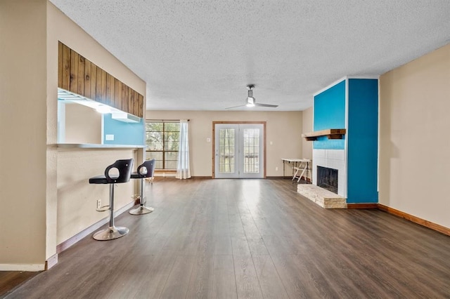 unfurnished living room featuring a tile fireplace, ceiling fan, a textured ceiling, dark hardwood / wood-style flooring, and french doors