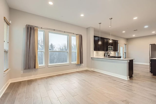 kitchen with decorative light fixtures, kitchen peninsula, sink, and light hardwood / wood-style flooring