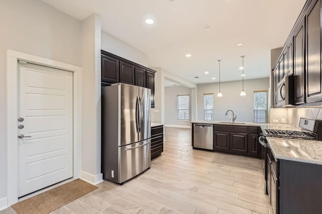 kitchen featuring sink, appliances with stainless steel finishes, hanging light fixtures, light hardwood / wood-style floors, and light stone countertops