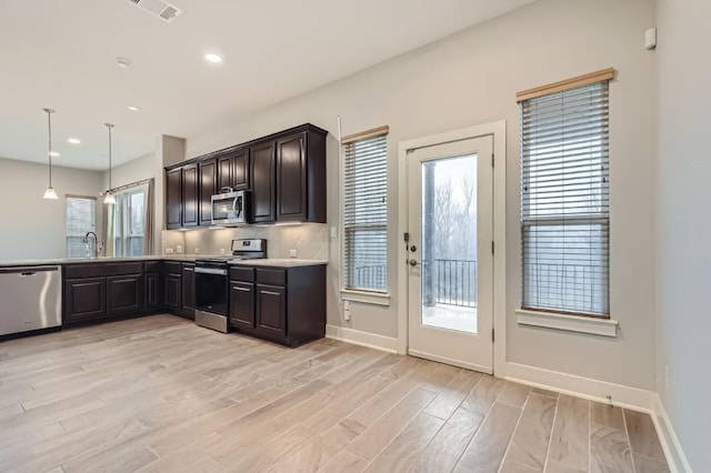 kitchen featuring sink, decorative light fixtures, light hardwood / wood-style flooring, appliances with stainless steel finishes, and backsplash