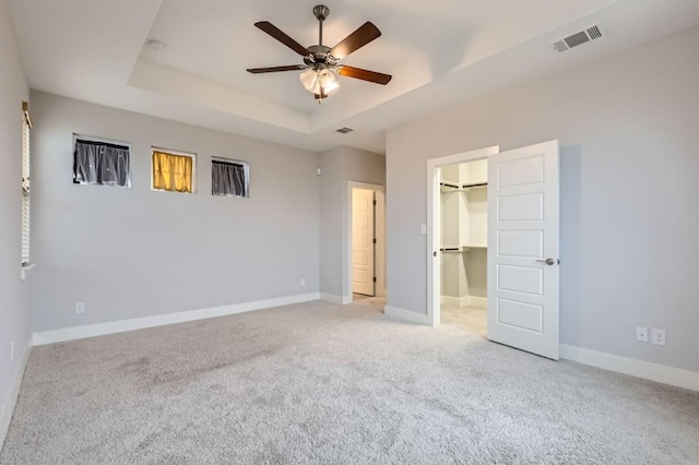 unfurnished bedroom with a walk in closet, light carpet, a raised ceiling, a closet, and ceiling fan