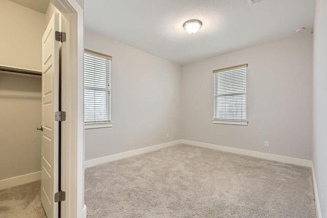 unfurnished bedroom with multiple windows, a spacious closet, and light carpet