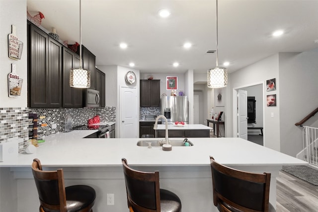 kitchen with sink, a breakfast bar area, hanging light fixtures, dark brown cabinetry, and stainless steel appliances