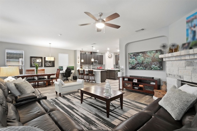 living room featuring a stone fireplace, light hardwood / wood-style floors, and ceiling fan