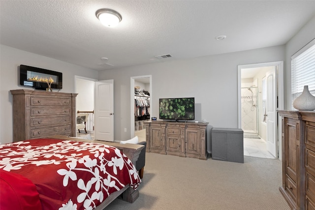 bedroom featuring connected bathroom, a textured ceiling, a spacious closet, light colored carpet, and a closet