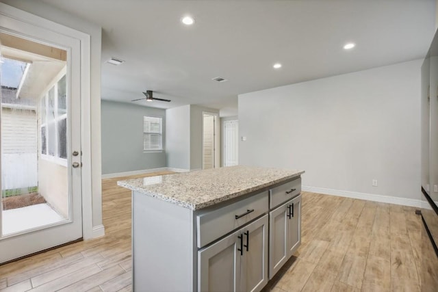 kitchen with gray cabinets, ceiling fan, light stone counters, light hardwood / wood-style floors, and a kitchen island