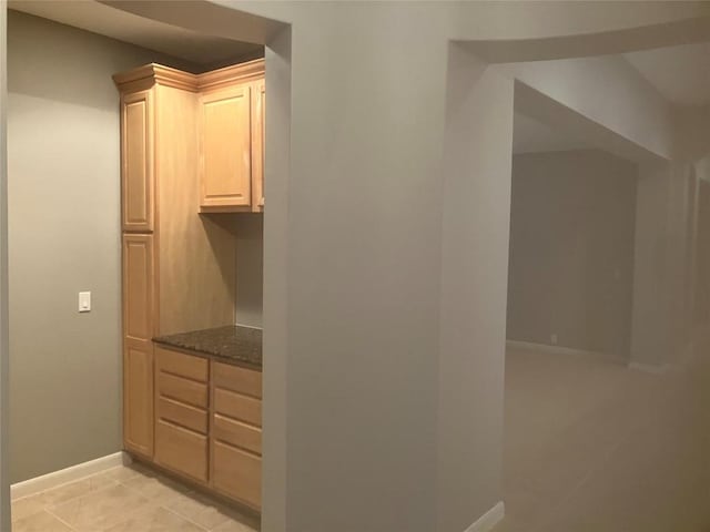 interior space featuring light tile patterned flooring, light brown cabinetry, and dark stone counters