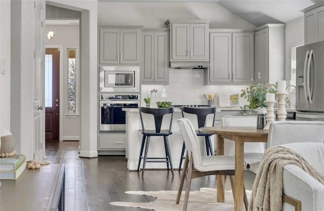 kitchen with dark wood-type flooring, lofted ceiling, appliances with stainless steel finishes, gray cabinets, and decorative backsplash