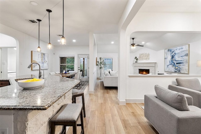 kitchen with sink, stone countertops, decorative light fixtures, and a kitchen island with sink