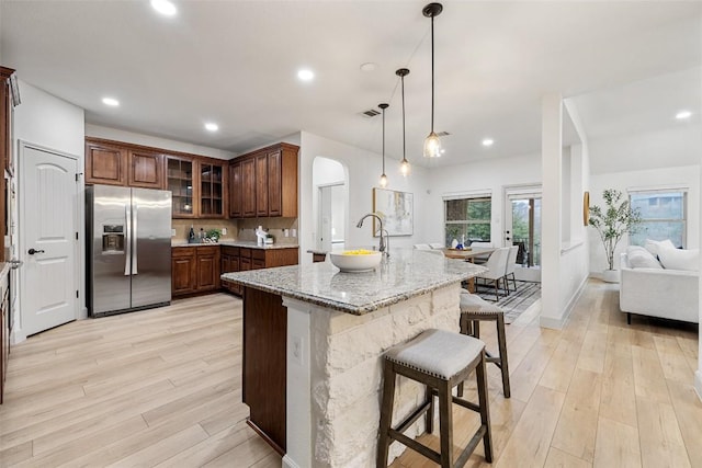 kitchen with pendant lighting, stainless steel fridge, a kitchen bar, light stone countertops, and a center island with sink