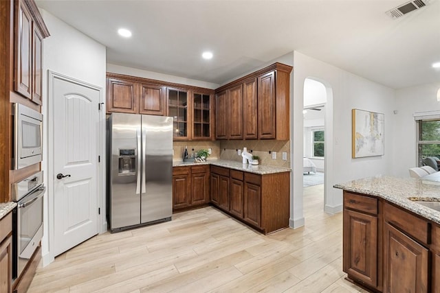 kitchen featuring sink, stainless steel appliances, light stone counters, decorative backsplash, and light wood-type flooring