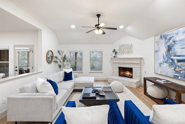 living room featuring ceiling fan, a stone fireplace, vaulted ceiling, and light hardwood / wood-style flooring