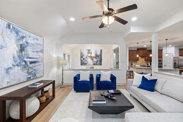 living room featuring ceiling fan with notable chandelier and light hardwood / wood-style flooring