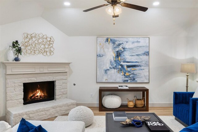 living room featuring a fireplace, light hardwood / wood-style floors, ceiling fan, and vaulted ceiling