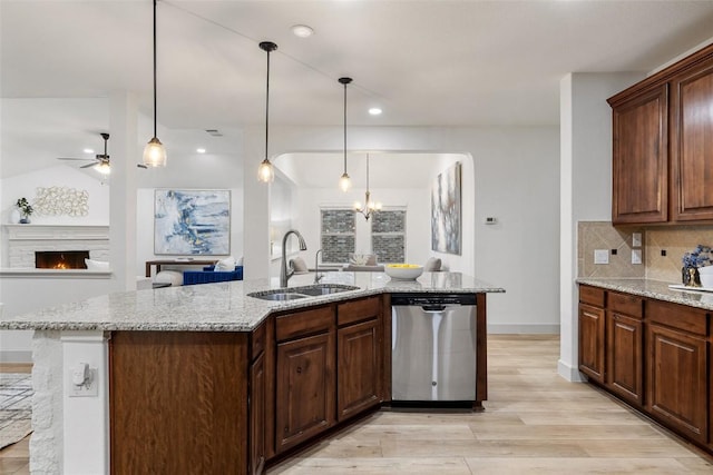 kitchen featuring tasteful backsplash, sink, a kitchen island with sink, stainless steel dishwasher, and light stone counters