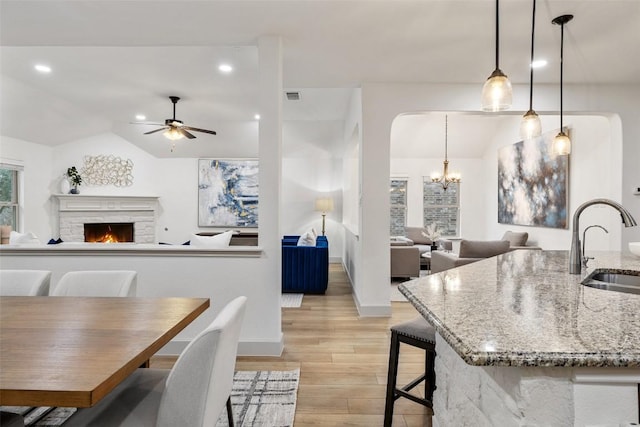 kitchen featuring a stone fireplace, lofted ceiling, sink, hanging light fixtures, and light stone counters