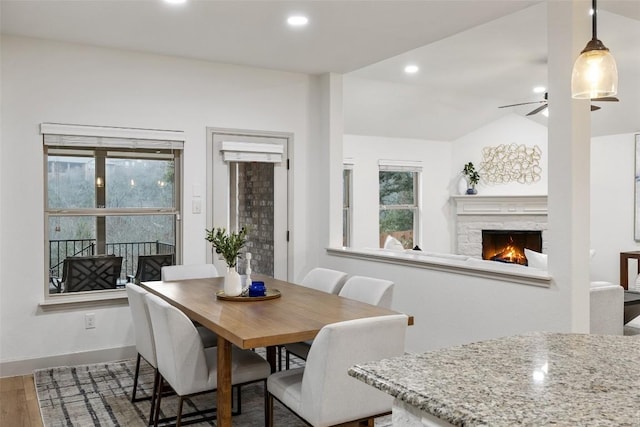 dining area featuring hardwood / wood-style flooring, ceiling fan, lofted ceiling, and a fireplace