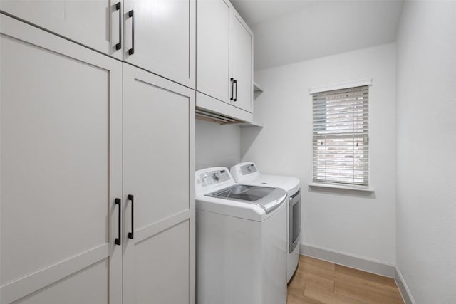 clothes washing area with cabinets, washer and dryer, and light wood-type flooring