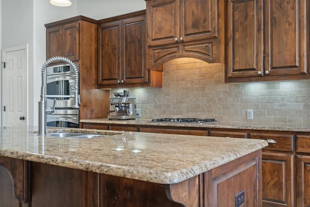 kitchen featuring light stone countertops, sink, a center island with sink, and backsplash