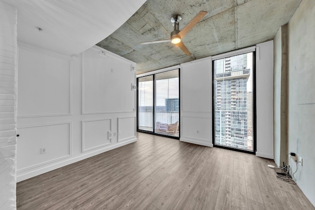 empty room with floor to ceiling windows, ceiling fan, and light hardwood / wood-style floors