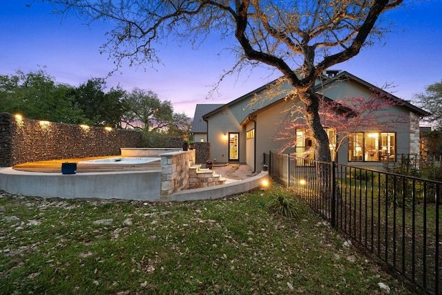 property exterior at dusk with a jacuzzi, a lawn, and a fenced backyard