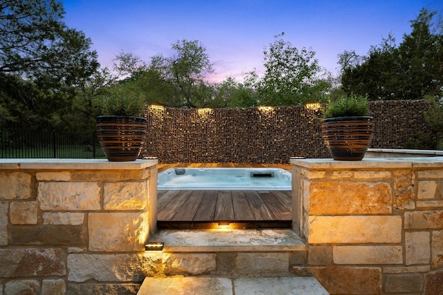 pool at dusk with fence and a hot tub