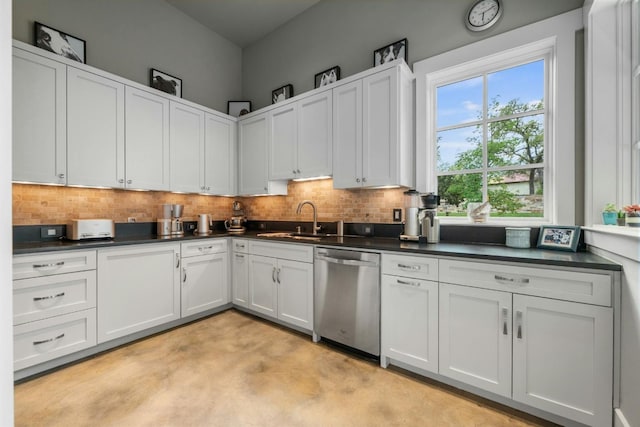 kitchen with stainless steel dishwasher, dark countertops, a sink, and tasteful backsplash