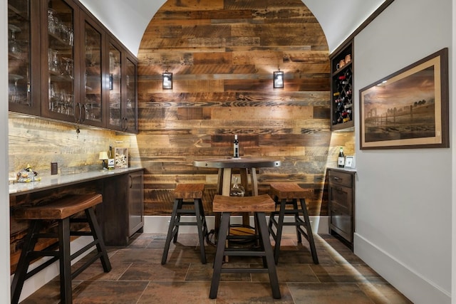 bar featuring stone finish flooring, indoor bar, wood walls, and baseboards