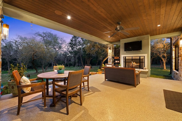 view of patio featuring outdoor dining space, ceiling fan, and a lit fireplace